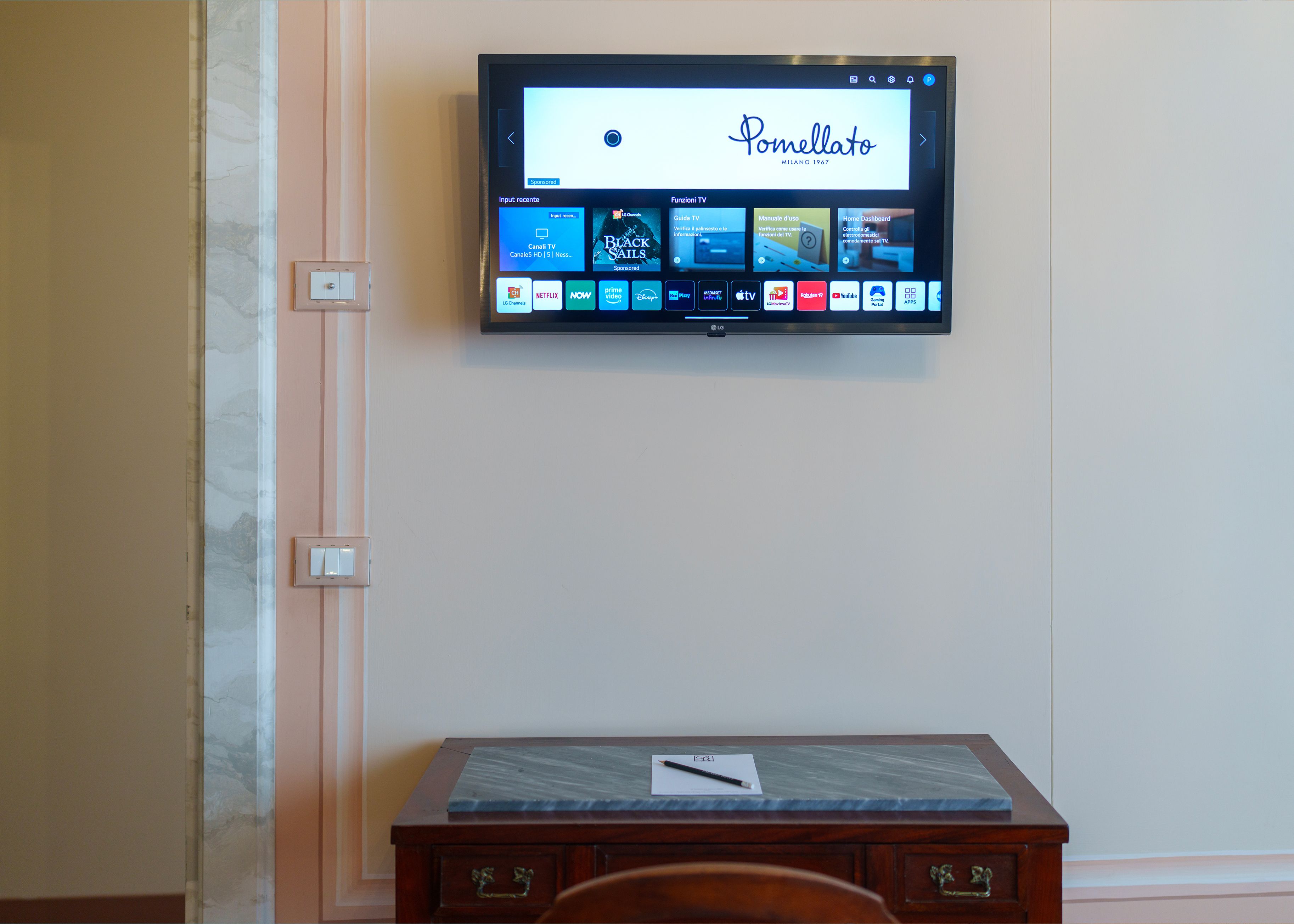 A flat-screen TV mounted on a wall displaying the Pommellato menu.