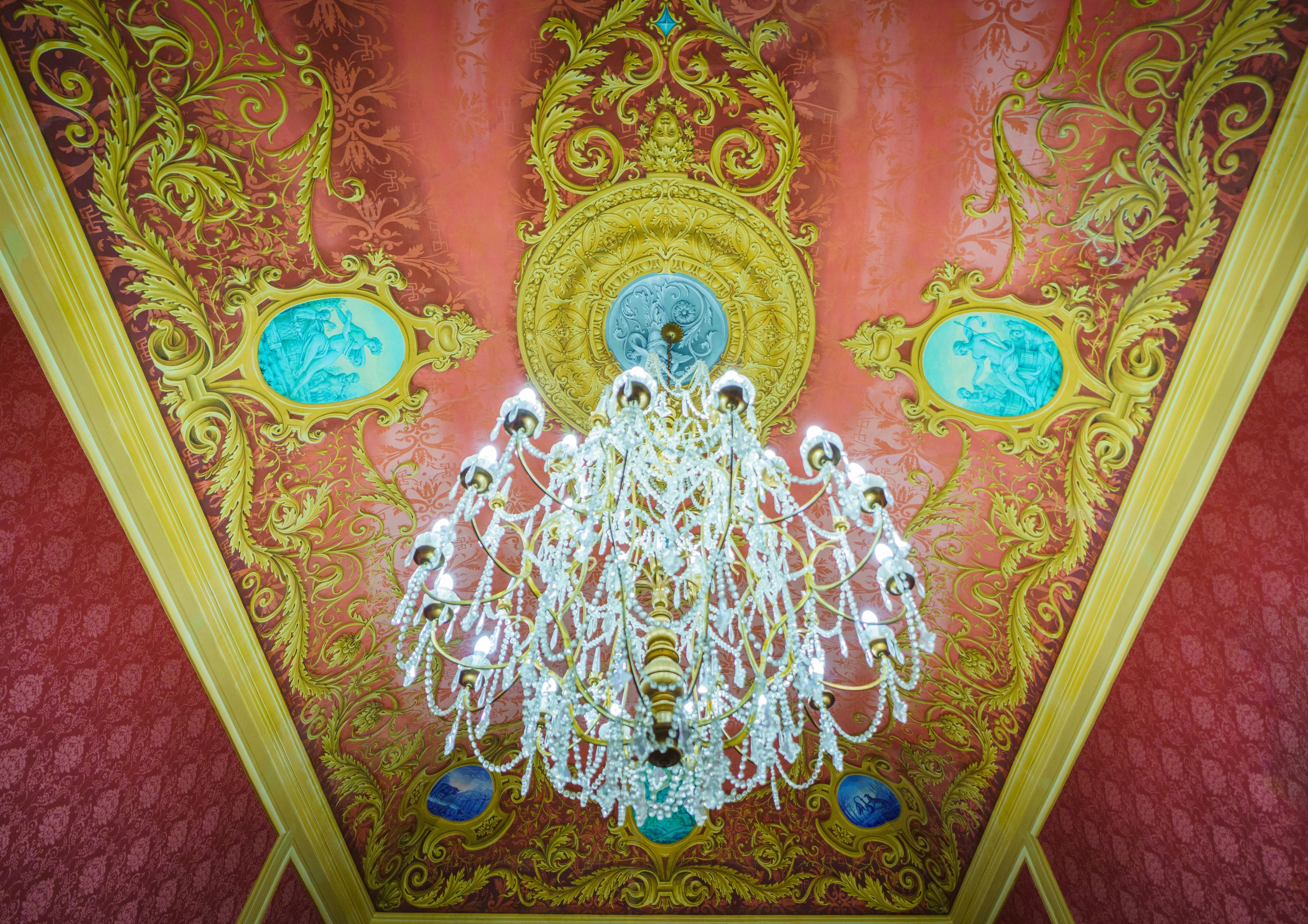 A ceiling with ornate gold and blue designs, a chandelier, and a central medallion.