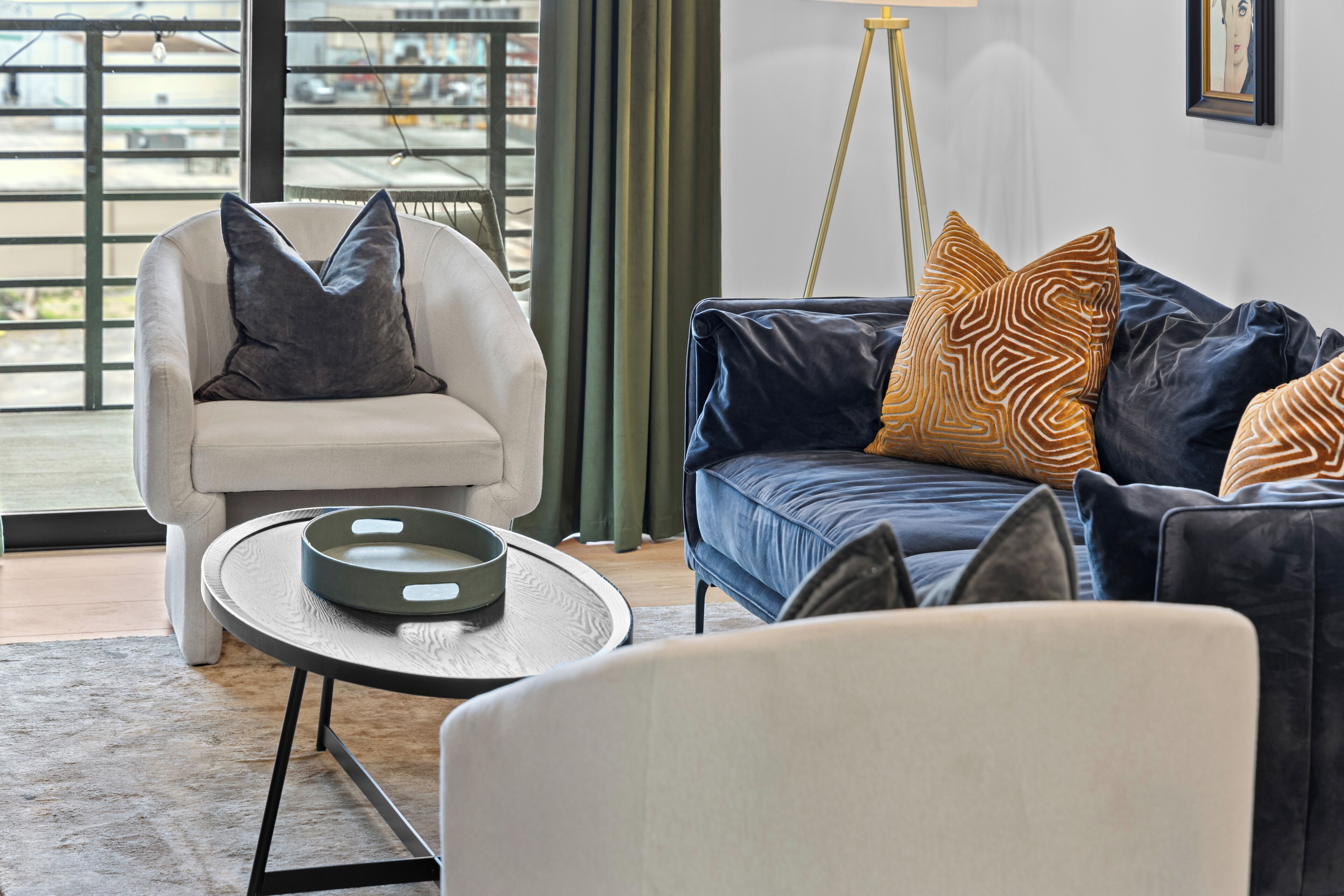 Una sala de estar moderna con un sillón blanco, un sofá azul con cojines estampados y una mesa redonda de centro.