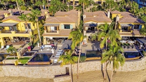 Un hotel sulla spiaggia con diversi edifici, una piscina e palme.