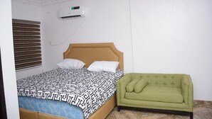 A bedroom with a bed, a green armchair, and an air conditioning unit on the wall. - Highcon Hotel and Suite (Omu-Aran)