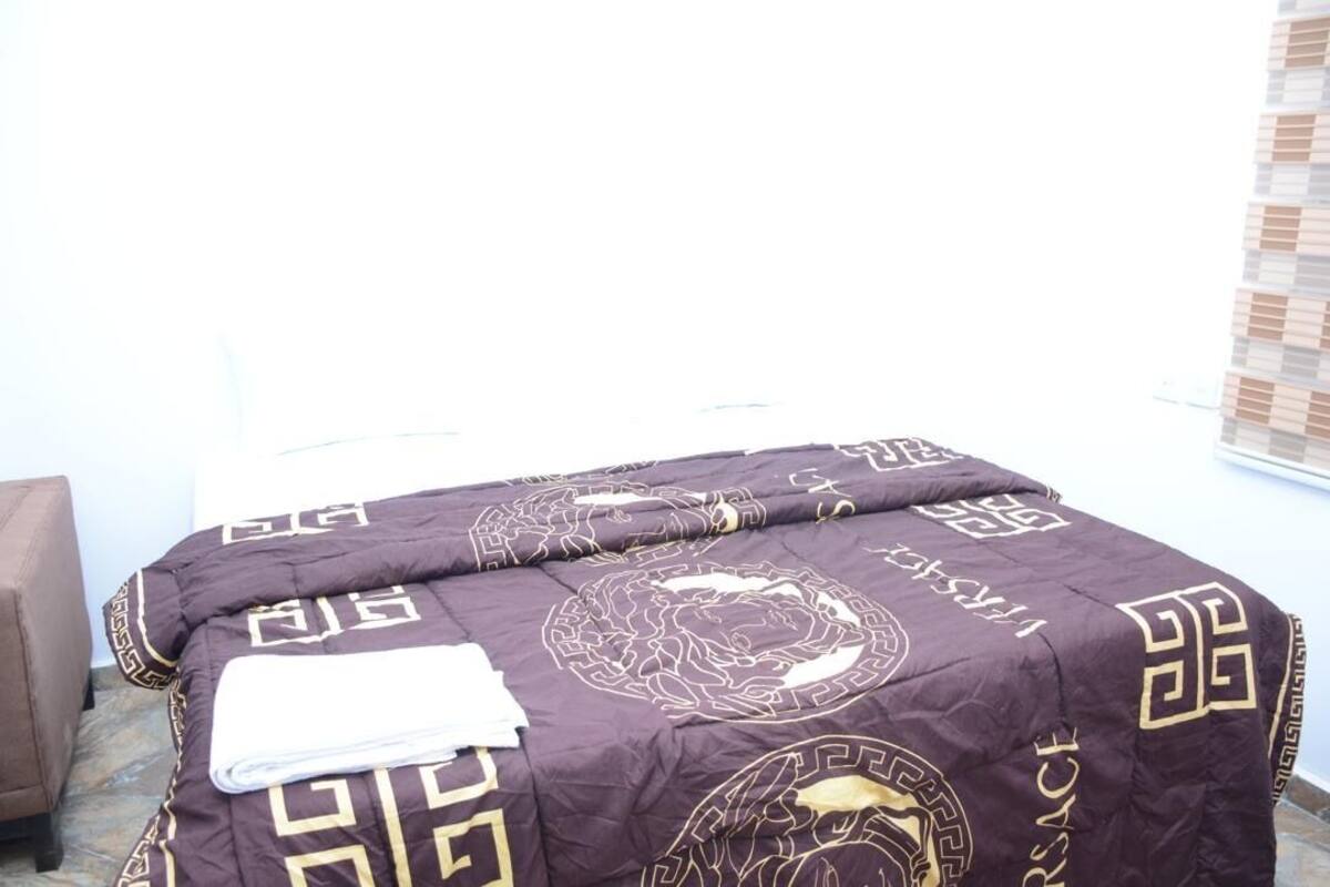 A bed with a dark patterned bedspread and a white pillow.