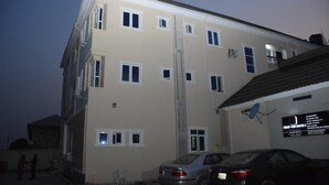 A multi-story building with a central stairwell, several windows, and a parked car in front. - Highcon Hotel and Suite (Omu-Aran)