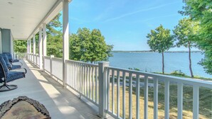 A covered porch with a view of a lake, a wooden table, and blue chairs. - Modern Lakeside Retreat on Lake Ontario 4+ bedroom/3 bath (Dexter)