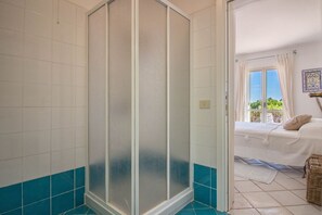 Ein Badezimmer mit Dusche, ein Bett mit Blick und ein Fenster mit Vorhängen.