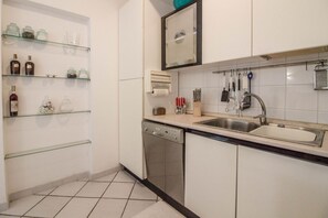 Una cocina con armarios blancos, lavavajillas, fregadero y repisas de vidrio con frascos.