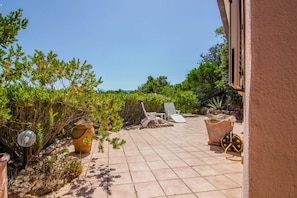 Une terrasse avec un sol carrelé, des plantes en pot et deux fauteuils de jardin.