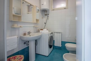 Ein Badezimmer mit Waschbecken, Spiegel, Handtuchhalter, Waschmaschine, Toilette und Radiator.