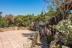 A stone pathway leading to a circular patio area surrounded by greenery and a stone wall.