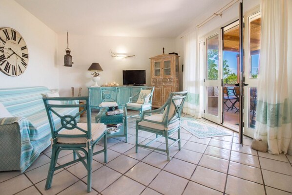 A living room with a sofa, chairs, a television, a cabinet, and a sliding glass door leading to an outdoor area.