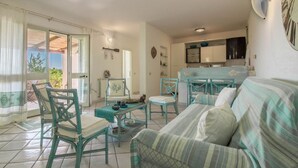 Una sala de estar con sofá, sillas, una mesa y una cocina con armarios y encimera.