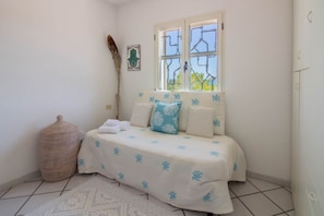 Une chambre à coucher avec un lit, une fenêtre, un panier en osier et un objet décoratif fixé au mur.
