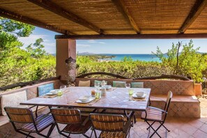 Een terras met een tafel voor vier personen, omringd door zachte zitplaatsen, met uitzicht op zee en groen.