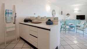 Una cocina con una isla central, un comedor con sillas, un televisor y un reloj en la pared.