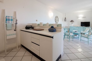 Une cuisine dotée d’un îlot central, un coin repas avec des chaises, un téléviseur et une horloge au mur.