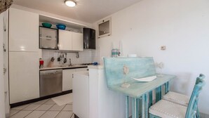 Una cocina compacta con armarios blancos, lavavajillas y un pequeño comedor con una mesa y una silla azules.