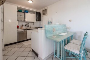 A compact kitchen with white cabinets, a dishwasher, and a small dining area with a blue table and chair.