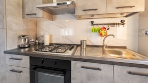 Een moderne keuken met een gasfornuis, een roestvrijstalen spoelbak en een marmeren spatwand.