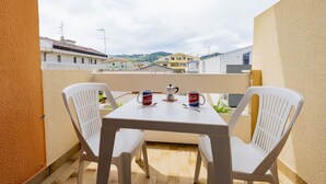 Een balkon met een tafel en twee stoelen, een koffiezetapparaat en twee Coca-Cola mokken.