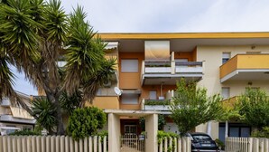 Een meerlaags appartementencomplex met balkons, een hekpoort en een geparkeerde auto.