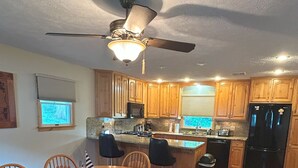 A kitchen with wooden cabinets, a dining table with chairs, a ceiling fan, and a view of the outdoors through a window. - Pristine 3-bedroom cottage in Lakeside, Ohio with central air, laundry, Wi-Fi (Lakeside)