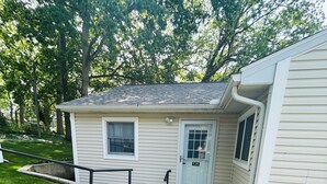 A single-story house with a front door, a small window, and a visible garage door. - Pristine 3-bedroom cottage in Lakeside, Ohio with central air, laundry, Wi-Fi (Lakeside)