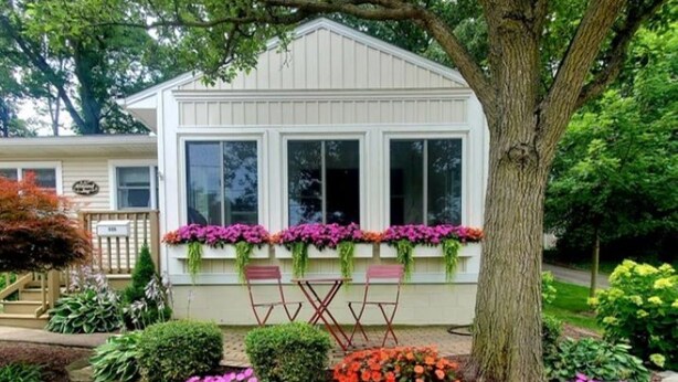 A white house with large windows and a stone border around the garden. - Pristine 3-bedroom cottage in Lakeside, Ohio with central air, laundry, Wi-Fi (Lakeside)