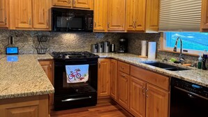 A kitchen with wooden cabinets, granite countertops, a black stove, and a window with blinds. - Pristine 3-bedroom cottage in Lakeside, Ohio with central air, laundry, Wi-Fi (Lakeside)