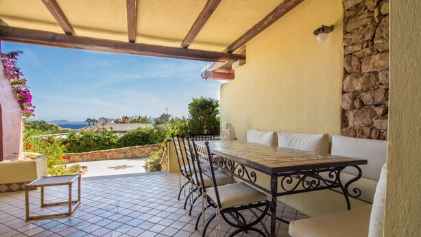 An outdoor patio with a table and chairs, a stone wall, and a view of the landscape. - GuestHost - Seaview Villa with Veranda GolfoAranci (Golfo Aranci)
