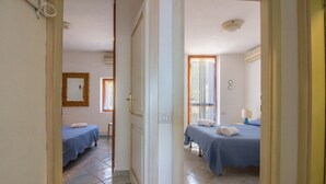 A hotel room with two beds, a window with curtains, a bedside table with a lamp, and a door leading to another room. - GuestHost - Seaview Villa with Veranda GolfoAranci (Golfo Aranci)