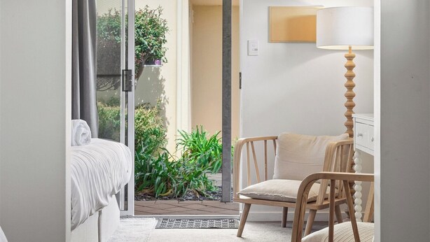 A hotel room with a bed, a chair, a lamp, and a view of a garden through a sliding door.