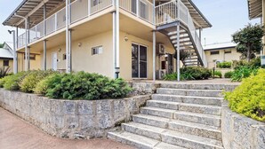 A two-story building with a balcony, a staircase, and a stone retaining wall.