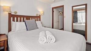 A hotel room with a large bed, two wall-mounted lamps, a wooden headboard, a mirror, and a view of a balcony.