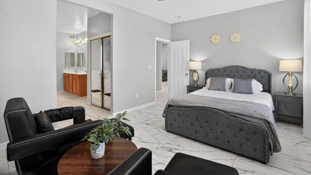 A bedroom with a bed, bedside lamps, a ceiling fan, and a bathroom visible through an open door.
