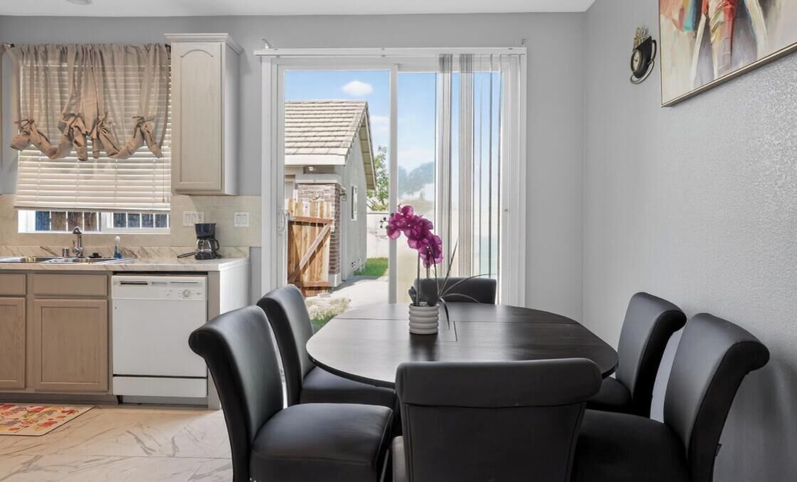 Zona pranzo con tavolo rotondo e sedie, cucina con lavastoviglie e vista su una casa tramite una porta scorrevole in vetro.