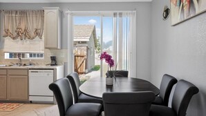 A dining area with a round table and chairs, a kitchen with a dishwasher, and a view of a house through a sliding glass door.