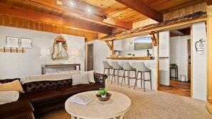 Una sala de estar acogedora con un sofá de cuero marrón, una mesa redonda y una zona de comedor con taburetes de bar.