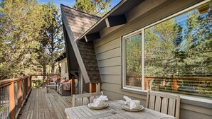 Terraza de madera con mobiliario exterior y un amplio ventanal con vista a un área boscosa.