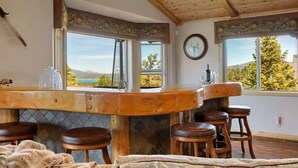 A rustic bar area with a wooden ceiling, a large window offering a scenic view, and a clock on the wall. - Treetop Oasis| Hot Tub, Lake Views, AC & Game Room (Big Bear Lake)