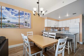 Una cocina moderna con armarios blancos, una isla central y un comedor con mesa de madera y sillas blancas.