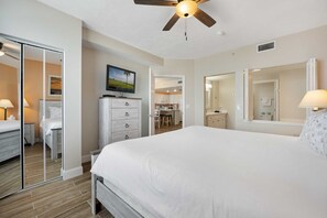 Un dormitorio con una cama grande, ventilador de techo, televisión, cómoda, espejo y vistas a la cocina.