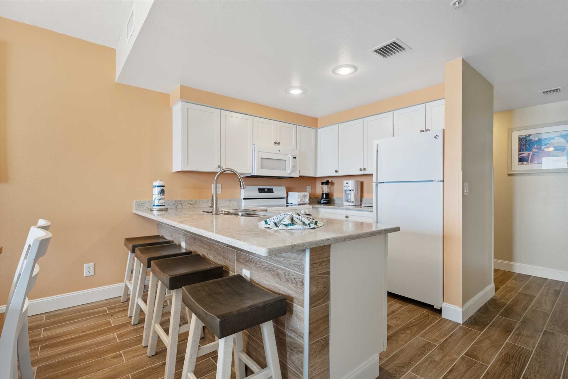 A modern kitchen with white cabinets, a central island with stools, a microwave, a refrigerator, and a coffee maker.