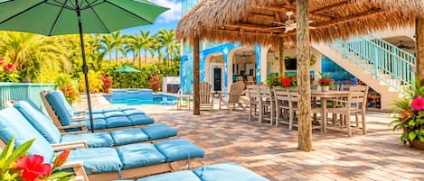 Un área junto a la piscina con sillones de descanso, una mesa de comedor y una estructura de techo de paja.