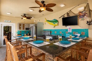 Une cuisine dotée d’un îlot central, de chaises en bois, de ventilateurs de plafond, d’un téléviseur et d’un poisson décoratif accroché au mur.