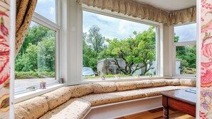 Una habitación con un banco empotrado junto a un amplio ventanal, que ofrece vistas a un jardín y una casa.
