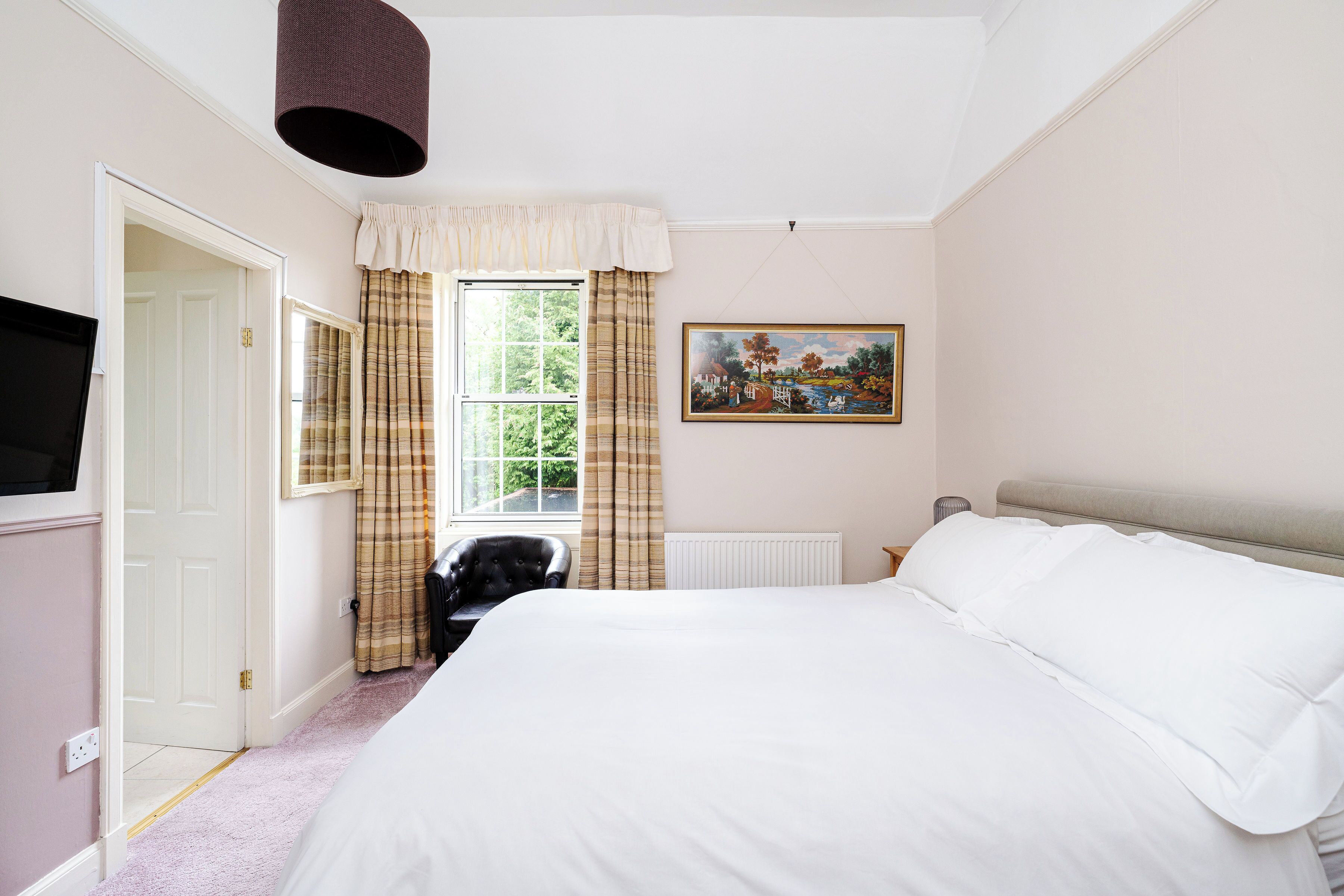 A bedroom with a bed, a window with curtains, a painting on the wall, and a television on the wall.
