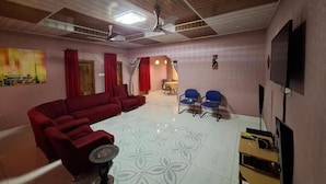A living room with a red sofa, blue chairs, a TV, and a ceiling fan. - Rankbel Holidays Apartment (Kumasi)