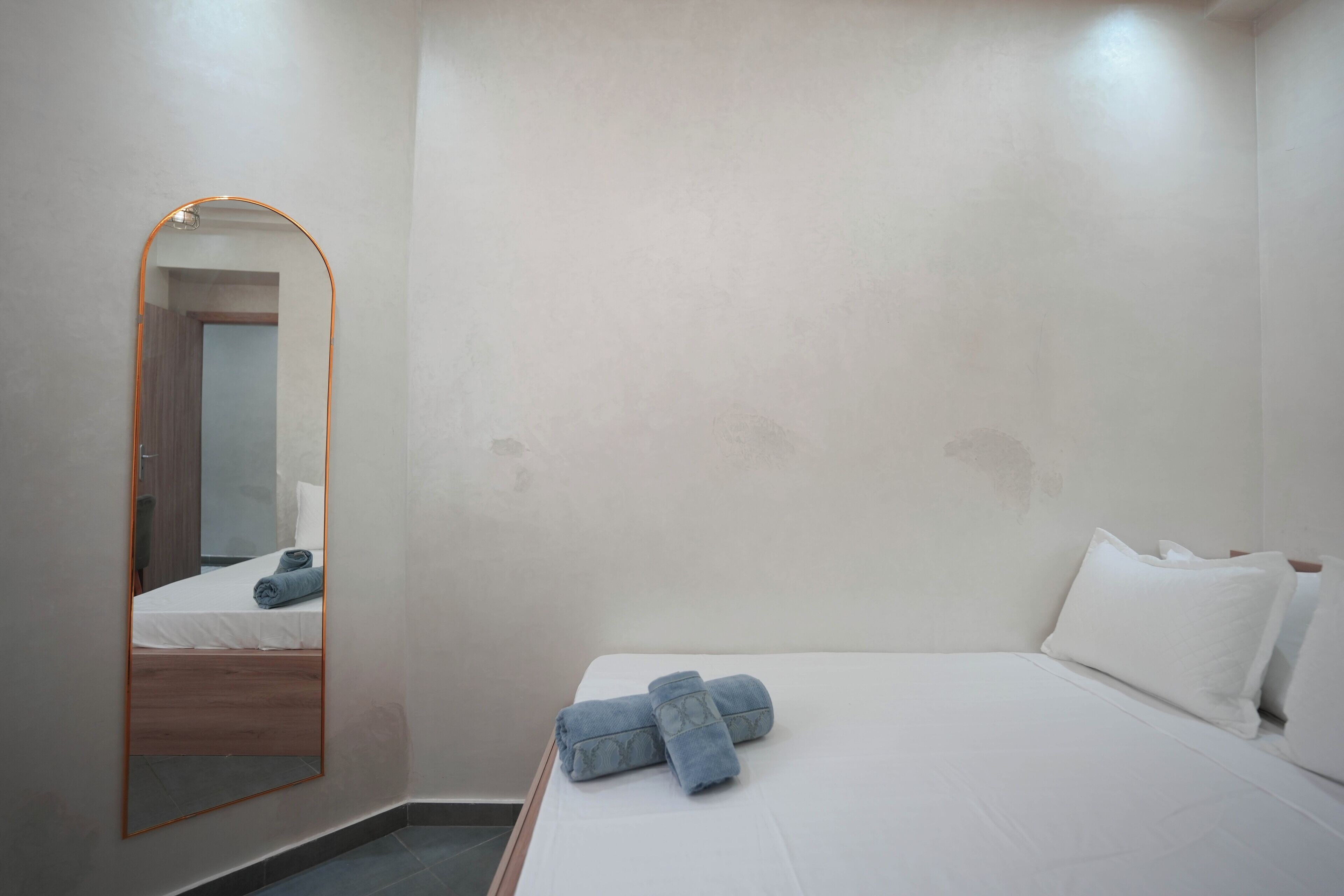 Habitación de hotel minimalista con un espejo grande, una cama bien hecha con sábanas blancas y un par de toallas dobladas.