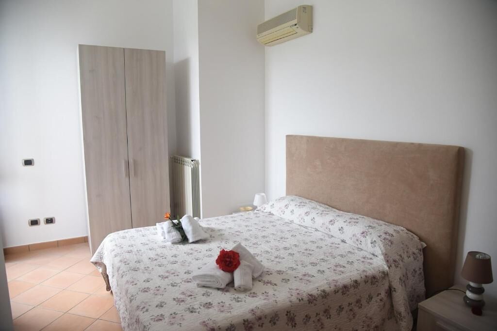 Habitació d'hotel amb un llit, una tauleta de nit, una làmpada, un radiador i un armari.
