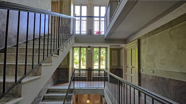 A grand staircase with marble steps and black railings, leading to a balcony with large windows and a view of greenery. - Anthea Domus (Sorrento)